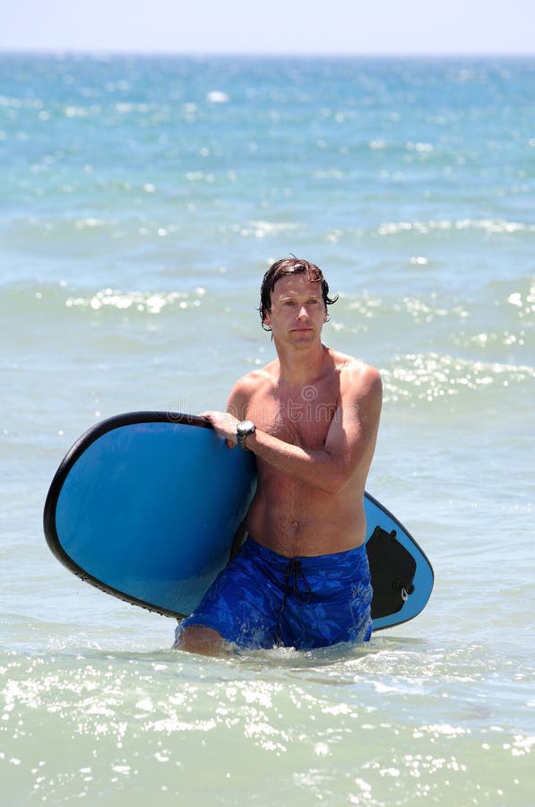 Handsome, fit middle aged man carrying surfboard on sandy beach in summer during vacation or holiday. Handsome, fit middle aged man carrying surfboard on sandy beach in summer during vacation or holiday