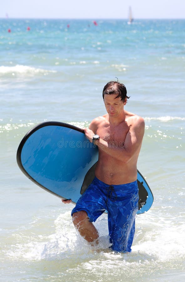 Handsome, fit middle aged man carrying surfboard on sandy beach in summer during vacation or holiday. Handsome, fit middle aged man carrying surfboard on sandy beach in summer during vacation or holiday