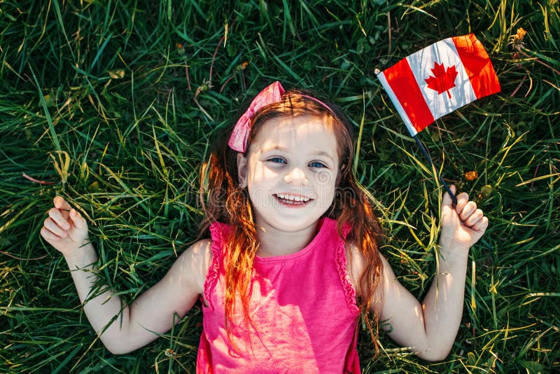 可爱快乐的白人女孩举着加拿大国旗 在公园草地上举着加拿大国旗的微笑孩子 儿童公民