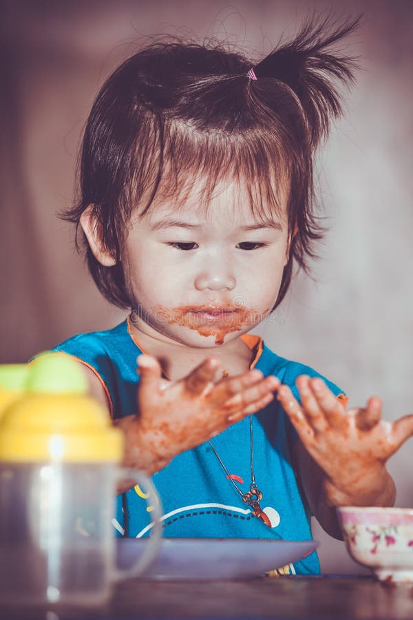 Portrait of a asian child enjoy eating. Her hand and mouth get stained with ketchup. Charming girl playing with food and learning to eat. Dirty face of happy kid. Do it yourself concept. Portrait of a asian child enjoy eating. Her hand and mouth get stained with ketchup. Charming girl playing with food and learning to eat. Dirty face of happy kid. Do it yourself concept.