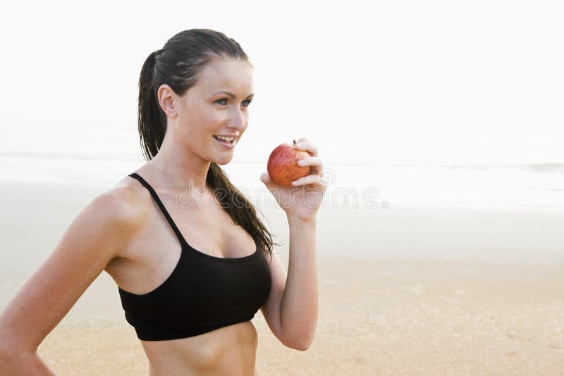 Side view of healthy fit young woman on beach eating apple. Side view of healthy fit young woman on beach eating apple