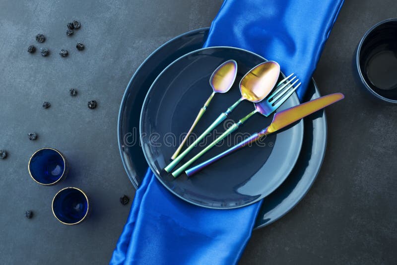 各种蓝色瓷盘,上面有蓝色桌布、金黄色蓝眼镜蓝莓和彩虹色餐具 免版税库存图片