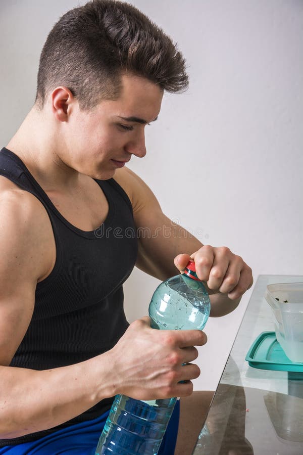 Hungry muscular young man gulping down food glancing across at the camera without pausing as he takes another mouthful. Hungry muscular young man gulping down food glancing across at the camera without pausing as he takes another mouthful