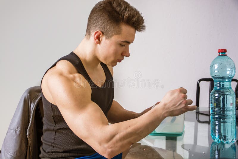 Hungry muscular young man gulping down food glancing across at the camera without pausing as he takes another mouthful. Hungry muscular young man gulping down food glancing across at the camera without pausing as he takes another mouthful