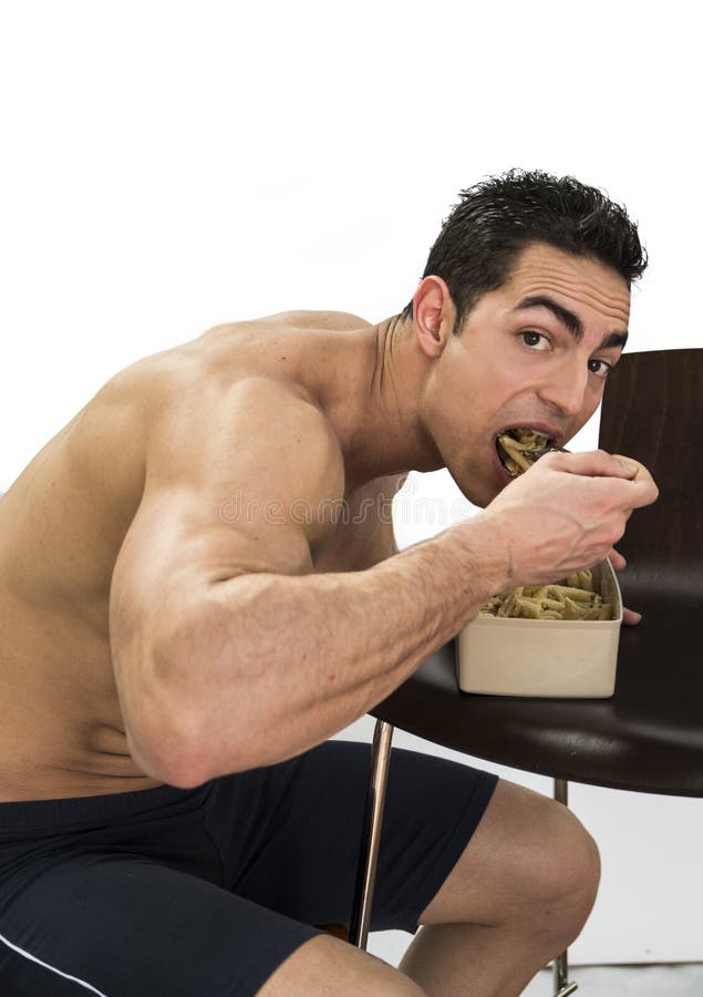 Hungry shirtless muscular young man gulping down food glancing across at the camera without pausing as he takes another mouthful. Hungry shirtless muscular young man gulping down food glancing across at the camera without pausing as he takes another mouthful