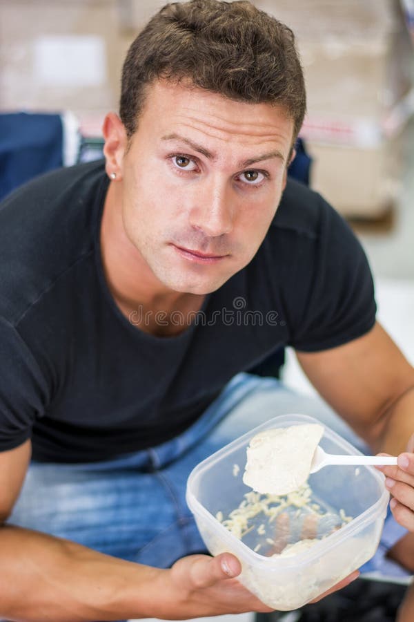 Hungry shirtless muscular young man gulping down food glancing across at the camera without pausing as he takes another mouthful. Hungry shirtless muscular young man gulping down food glancing across at the camera without pausing as he takes another mouthful