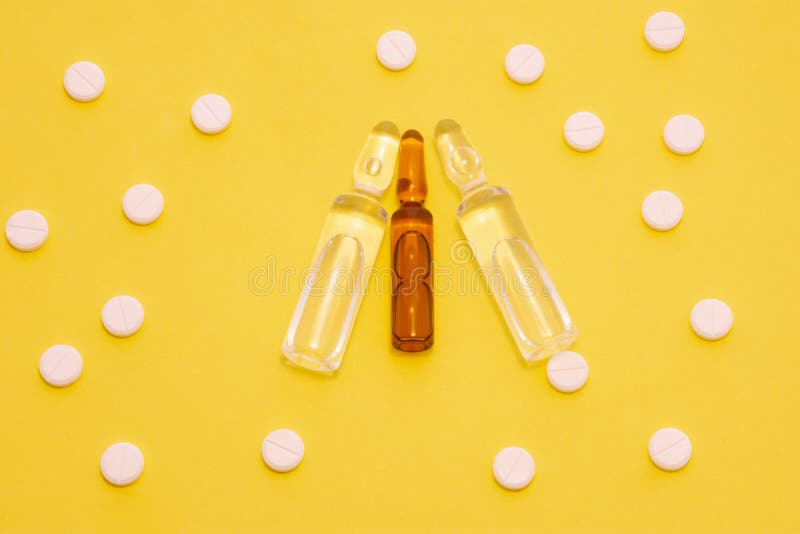 含药液的透明安瓿，在圆点图案的片周围呈黄色背景. 概念照片 免版税图库摄影