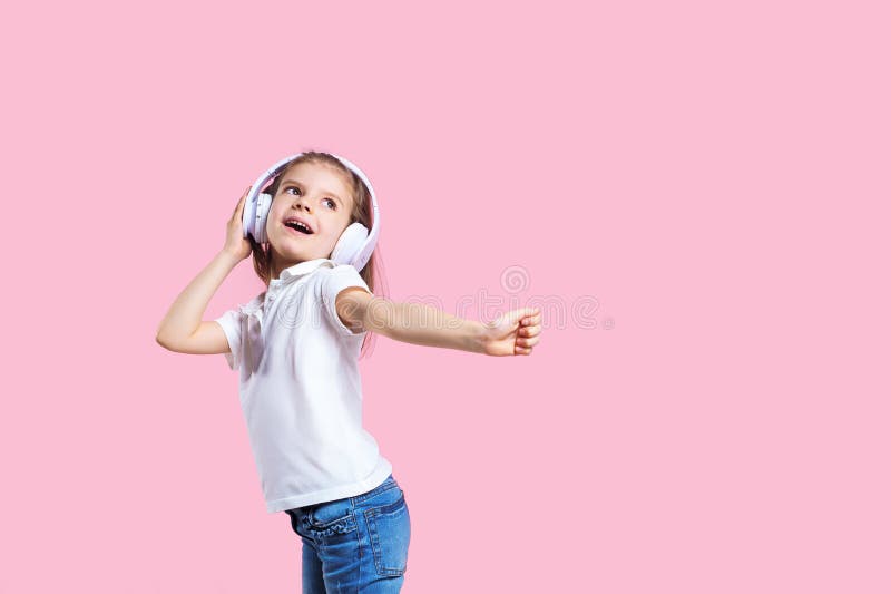 Girl listening to music in headphones on pink background. Cute child enjoying happy dance music, smile, posing on pink studio background wall. Girl listening to music in headphones on pink background. Cute child enjoying happy dance music, smile, posing on pink studio background wall.