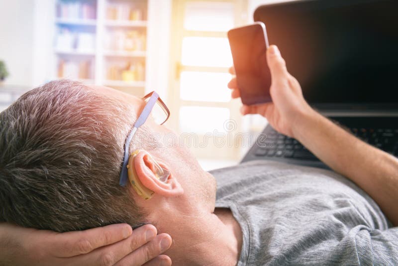 Hearing impaired man working with laptop and mobile phone at home. Hearing impaired man working with laptop and mobile phone at home