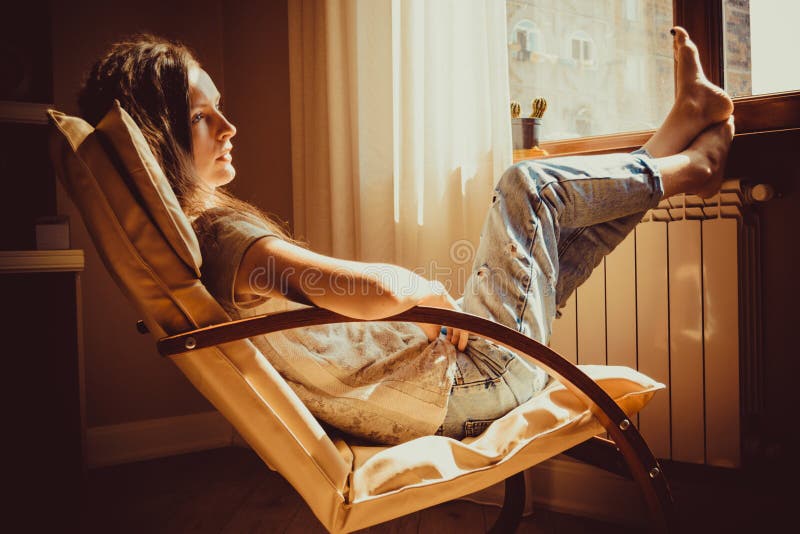 周道的概念 关闭在想法失去的画象哀伤的妇女lounging在舒适的现代椅子在窗口附近 温暖的自然lig 免版税库存图片