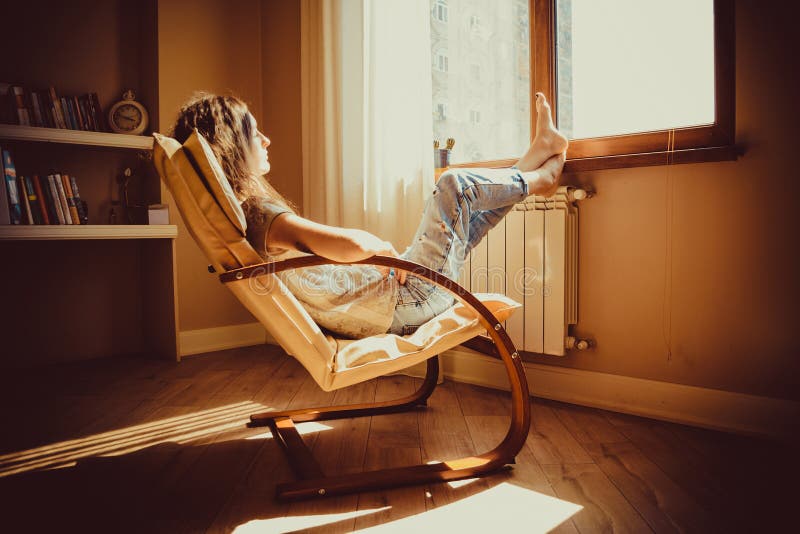 周道的概念 哀伤的妇女在想法丢失了lounging在看窗口的舒适的现代椅子在客厅 温暖的自然l 库存照片