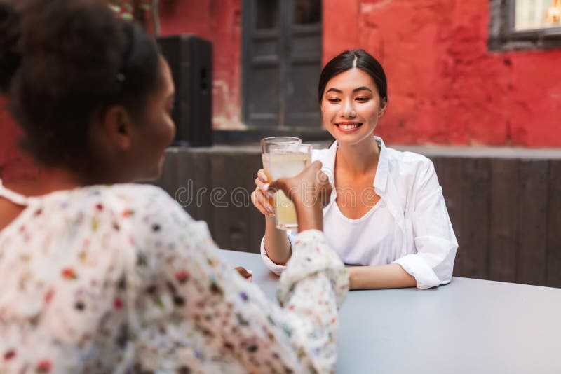 和朋友一起喝鸡尾酒的快乐的白衬衫女孩，在咖啡厅的庭院里快乐地度过时光 库存照片