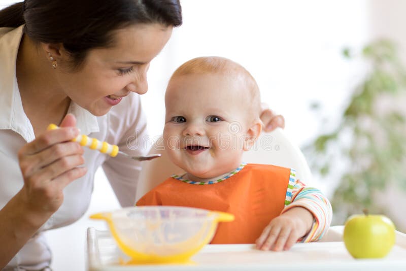 喂养她的有匙子的母亲婴孩 照顾在家给健康食物她可爱的孩子 库存照片 喂养她的有匙子的母亲婴孩 照顾在家给健康食物她可爱的孩子 库存照片