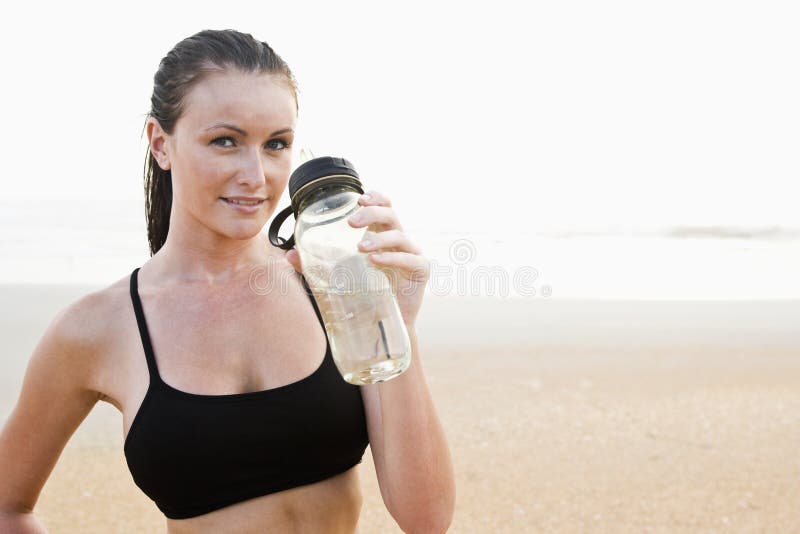 Front view of healthy fit young woman on beach drinking water. Front view of healthy fit young woman on beach drinking water