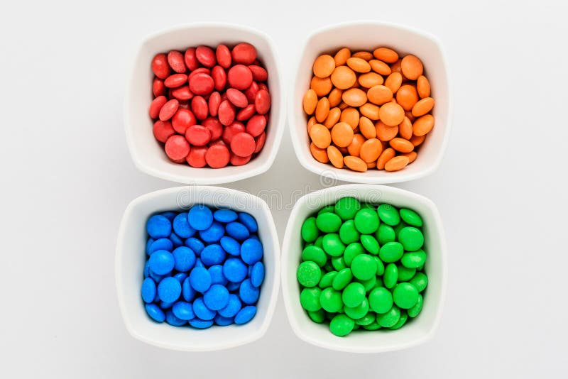 Four squared bowls with small red, yellow, blue, green and orange coated chocolate candies similar to m&ms in a squared bowl isolated on white background, top view. Four squared bowls with small red, yellow, blue, green and orange coated chocolate candies similar to m&ms in a squared bowl isolated on white background, top view