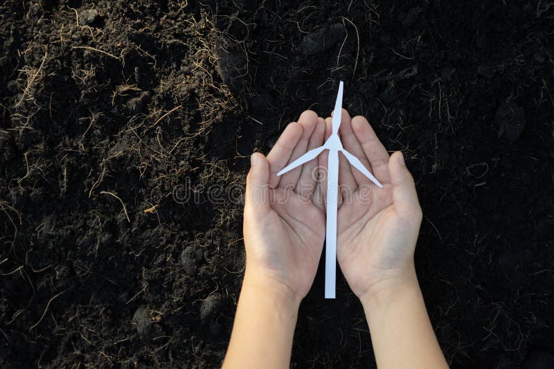 Hand holding wind turbine mockup or model over soil background top view to promote clean alternative energy source for future power sustainability and greener environment. Gyre. Hand holding wind turbine mockup or model over soil background top view to promote clean alternative energy source for future power sustainability and greener environment. Gyre