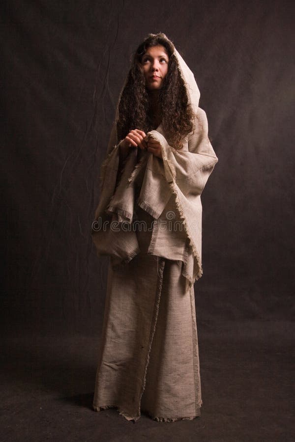 Closeup of religious young woman wearing biblical style gray robe, dark studio background. Closeup of religious young woman wearing biblical style gray robe, dark studio background.