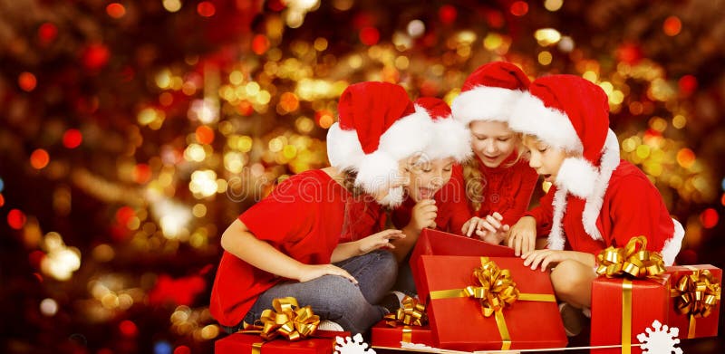 Christmas Kids Opening Present Gift Box, Happy Children in Santa Hat, Smiling Boys and Girls In Red Cap Funny Looking Toys. Christmas Kids Opening Present Gift Box, Happy Children in Santa Hat, Smiling Boys and Girls In Red Cap Funny Looking Toys