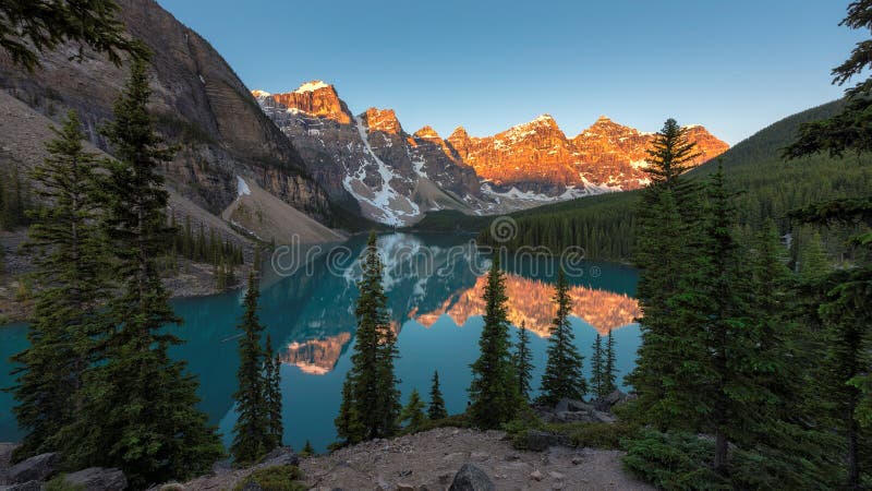 Beautiful sunrise under turquoise waters of the Moraine lake with snow-covered peaks above it in Banff National Park of Canada. Beautiful sunrise under turquoise waters of the Moraine lake with snow-covered peaks above it in Banff National Park of Canada.