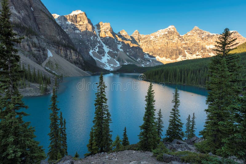 Beautiful sunrise under turquoise waters of the Moraine lake with snow-covered peaks above it in Canadian Rockies, Banff National Park of Canada. Beautiful sunrise under turquoise waters of the Moraine lake with snow-covered peaks above it in Canadian Rockies, Banff National Park of Canada.