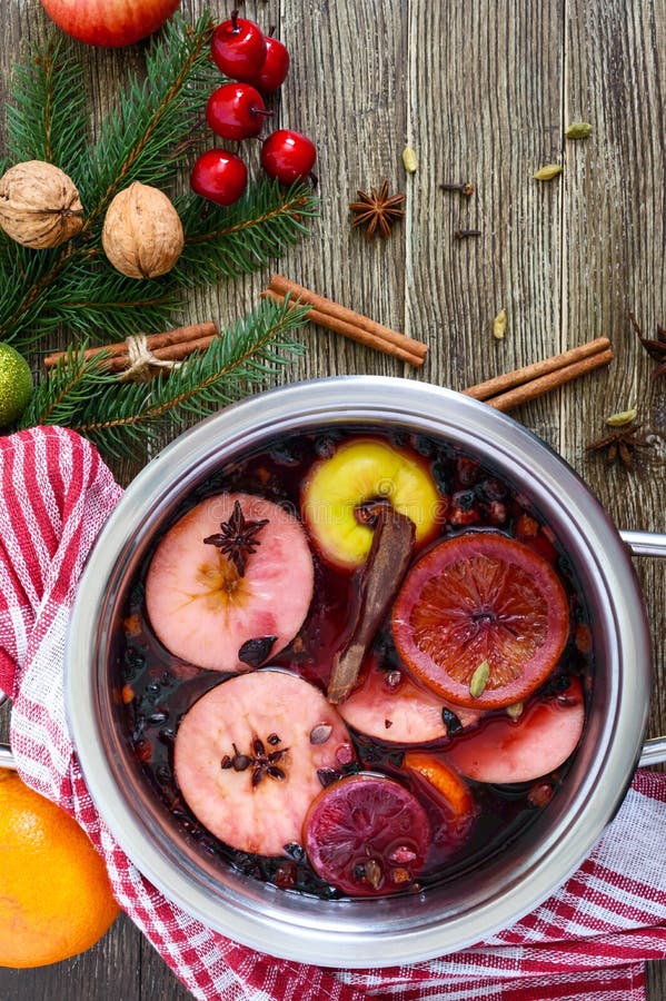 Hot mulled wine in a large pan on a wooden table. Fragrant traditional winter drink based on wine, juice, spices, seasonings, fruits. Top view. Hot mulled wine in a large pan on a wooden table. Fragrant traditional winter drink based on wine, juice, spices, seasonings, fruits. Top view