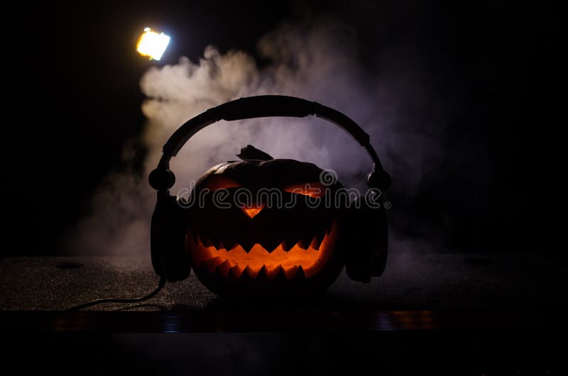 Halloween pumpkin on a dj table with headphones on dark background with copy space. Happy Halloween festival decorations and music concept. Halloween pumpkin on a dj table with headphones on dark background with copy space. Happy Halloween festival decorations and music concept