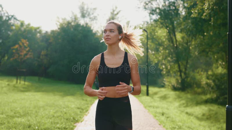 在公园里跑步的女运动员在户外训练时戴着耳机听音乐. 慢跑运动员 股票录像