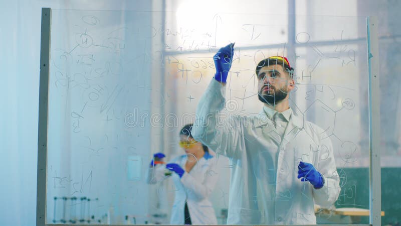 在化学实验室科学家男子化学配方的透明板背景上他的助理夫人 股票录像