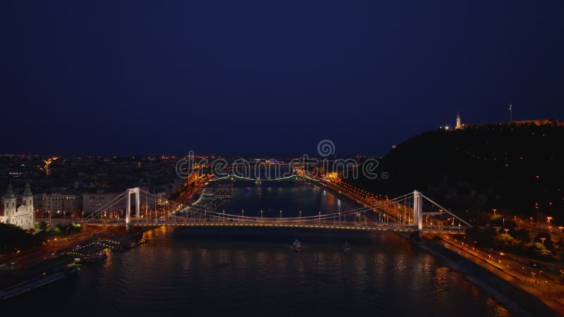 在大都市的夜间飞越宽多瑙河. 灯火通明的街道和桥梁. 布达佩斯