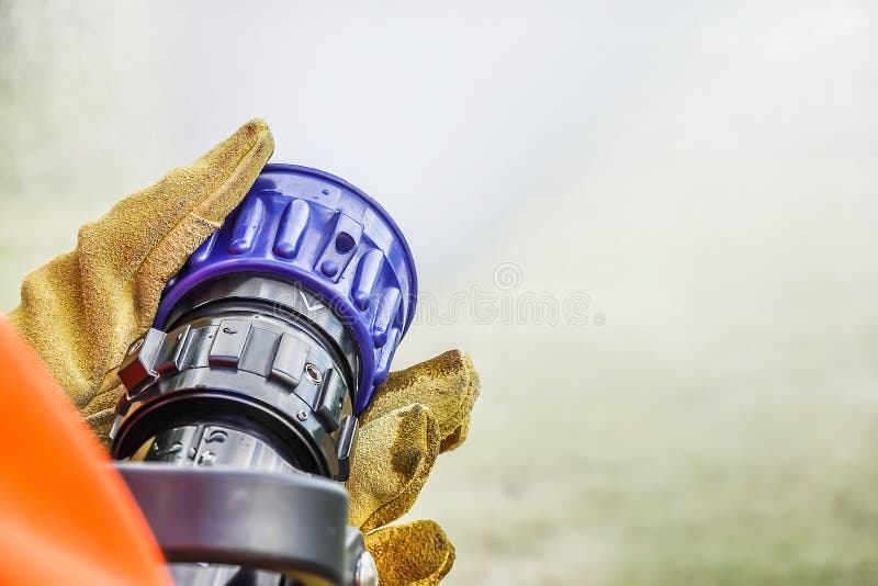 Two pairs of hands holding the handle on the end of a fire fighters water hose spraying water during practice at fire station. Two pairs of hands holding the handle on the end of a fire fighters water hose spraying water during practice at fire station