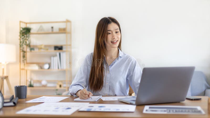 一位美丽的年轻亚洲女性正在家中观看老师在笔记本电脑上进行直播或视频通话教学 库存照片