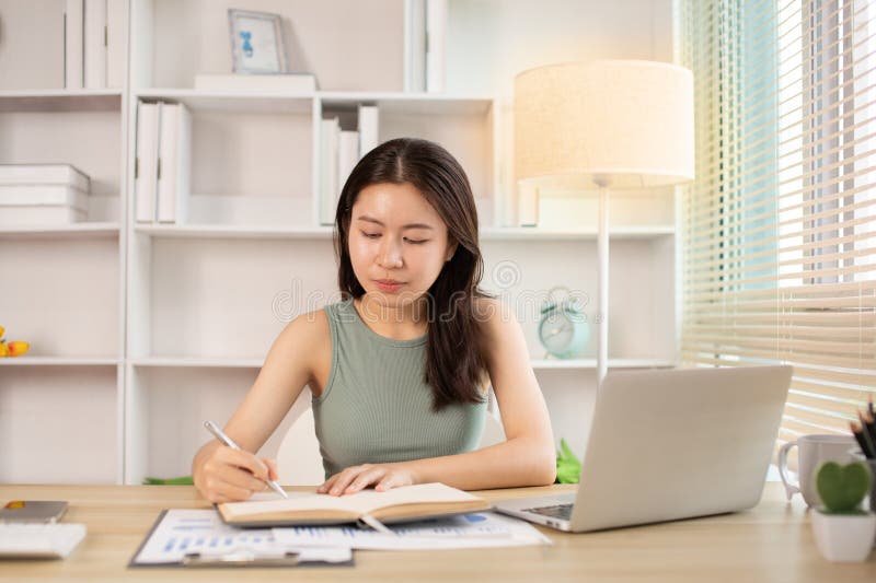 一位美丽的年轻亚洲女性在家中观看老师在笔记本电脑上进行教学的直播或视频通话 库存图片