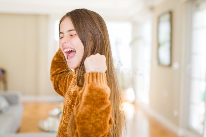 在家中，一个漂亮的小女孩激动地举起双臂庆祝胜利 图库摄影