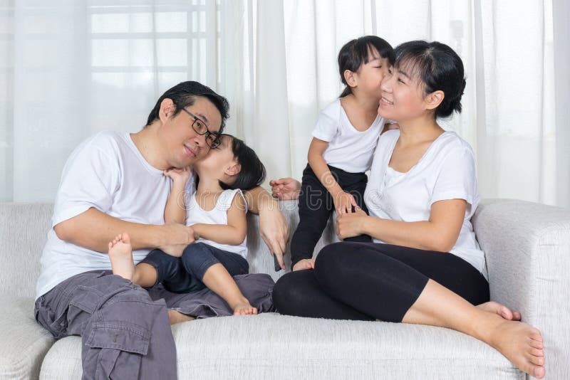 在家亲吻在长沙发的愉快的亚洲中国家庭 库存图片