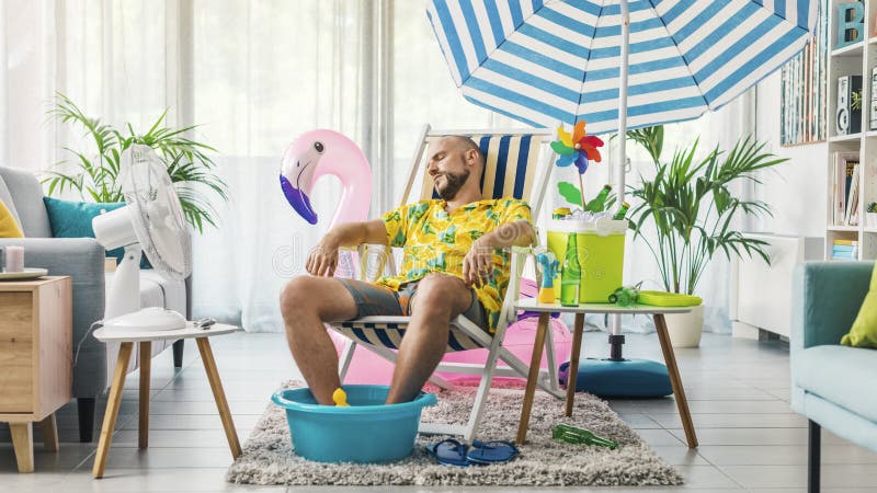 Man relaxing on a deckchair at home in the living room, he is having a staycation and pretending he is on a beach. Man relaxing on a deckchair at home in the living room, he is having a staycation and pretending he is on a beach