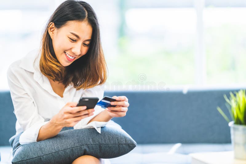 在家使用智能手机和信用卡的年轻美丽的亚裔妇女为网络购物与拷贝空间 E付款技术
