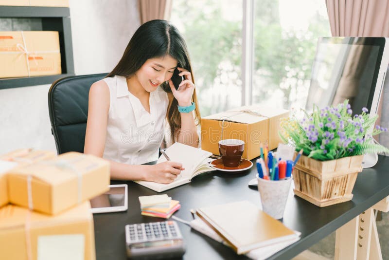 在家工作办公室，使用手机和注意关于购买订单的年轻亚洲小企业主