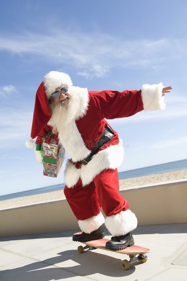 Happy Santa Claus skateboarding with gift in hand by beach against sky. Happy Santa Claus skateboarding with gift in hand by beach against sky