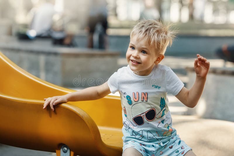 A cheerful,smiling,likeable little boy on the playground on a yellow slider. The child's hair is electrified and bristling. A cheerful,smiling,likeable little boy on the playground on a yellow slider. The child's hair is electrified and bristling.