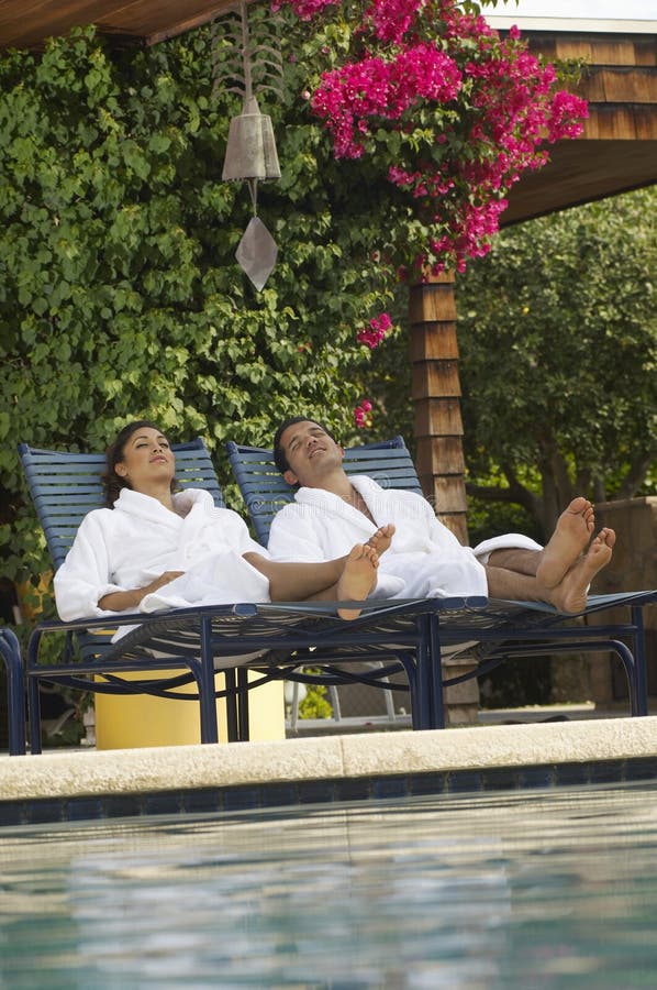 Young couple in bathrobes relaxing on deck chairs by swimming pool. Young couple in bathrobes relaxing on deck chairs by swimming pool