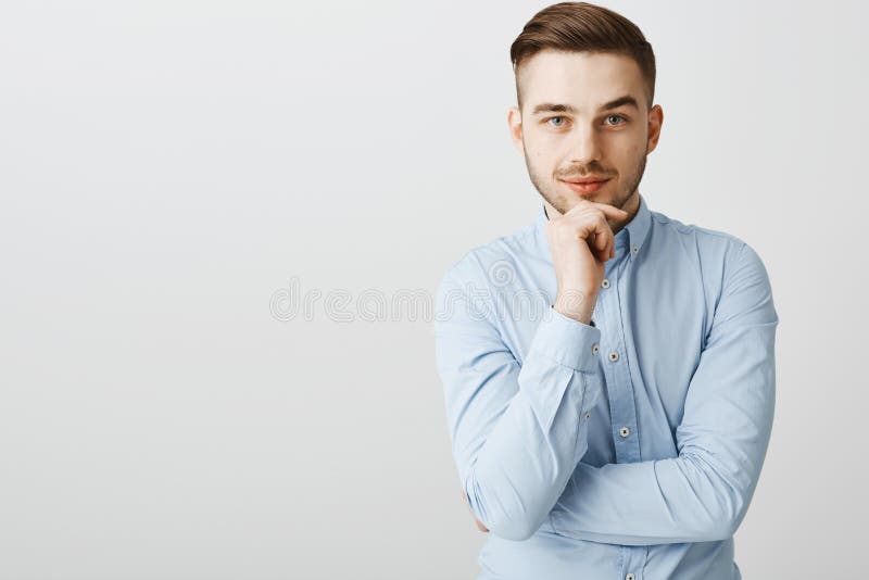 在时髦蓝领衬衣的聪明的雄心勃勃的英俊的男性握在下巴的手傻笑从兴趣和欢欣注视的 免版税库存照片 在时髦蓝领衬衣的聪明的雄心勃勃的英俊的男性握在下巴的手傻笑从兴趣和欢欣注视的 免版税库存照片