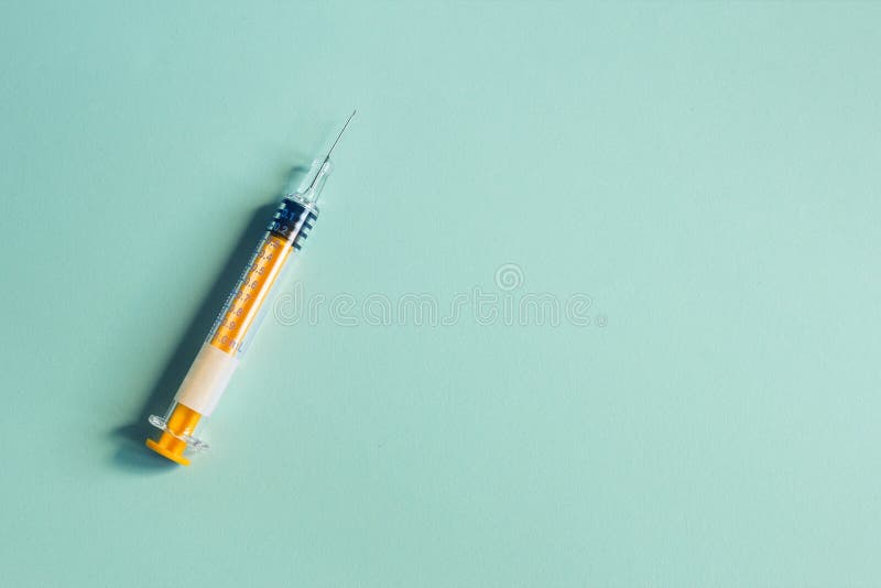 A colorful  syringe with the needle uncapped on textured bluish paper background and space to insert a text. Health sciences. Surgical aesthetics hospital medical material. A colorful  syringe with the needle uncapped on textured bluish paper background and space to insert a text. Health sciences. Surgical aesthetics hospital medical material