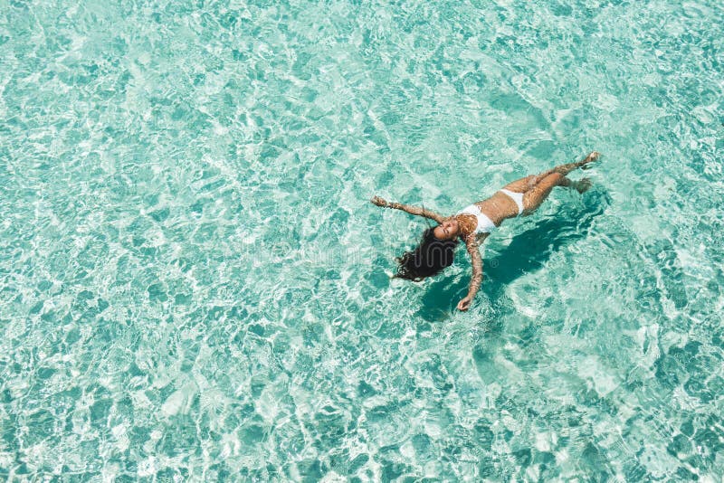 Woman in white bikini lying on transparent turquoise water surface on beach. Travel and vacations concept. Tropical background with empty space. Woman in white bikini lying on transparent turquoise water surface on beach. Travel and vacations concept. Tropical background with empty space