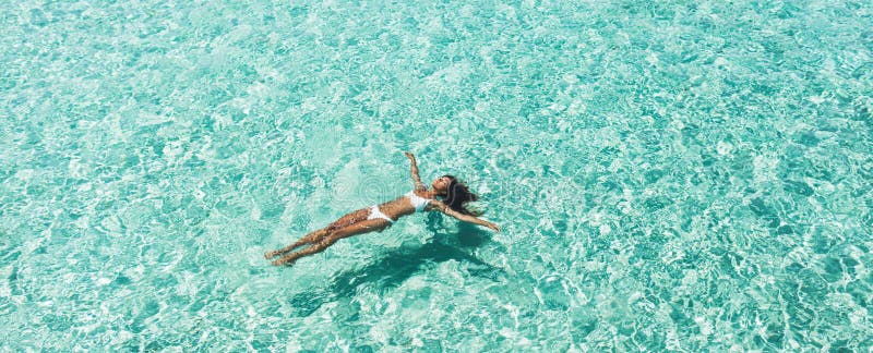 Woman in white bikini lying on transparent turquoise water surface on beach. Travel and vacations concept. Tropical background with empty space. Woman in white bikini lying on transparent turquoise water surface on beach. Travel and vacations concept. Tropical background with empty space