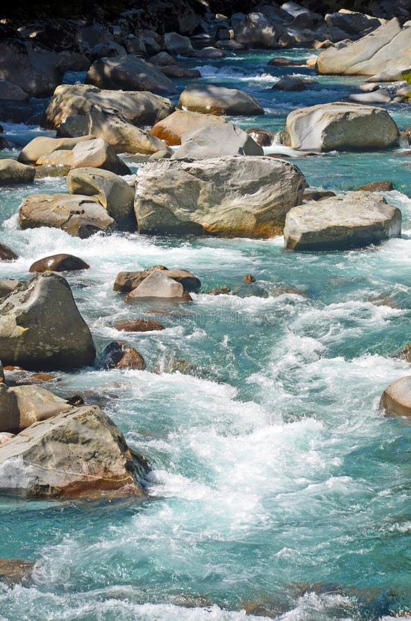 Crystal clear light blue alpine river water flowing as rapids through large boulders. Crystal clear light blue alpine river water flowing as rapids through large boulders.