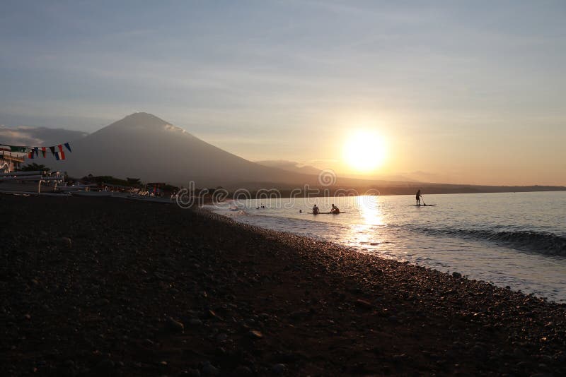 在沿海的浪漫日落在印度尼西亚 冲浪者去享用paddleboard在日落 有庄严火山的海岸线全景 库存照片 在沿海的浪漫日落在印度尼西亚 冲浪者去享用paddleboard在日落 有庄严火山的海岸线全景 库存照片