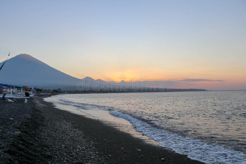 在海滩的日落在一个热带海岛上 桔黄色天空和云彩 在天际的大庄严火山 安静的海 免版税库存图片 在海滩的日落在一个热带海岛上 桔黄色天空和云彩 在天际的大庄严火山 安静的海 免版税库存图片