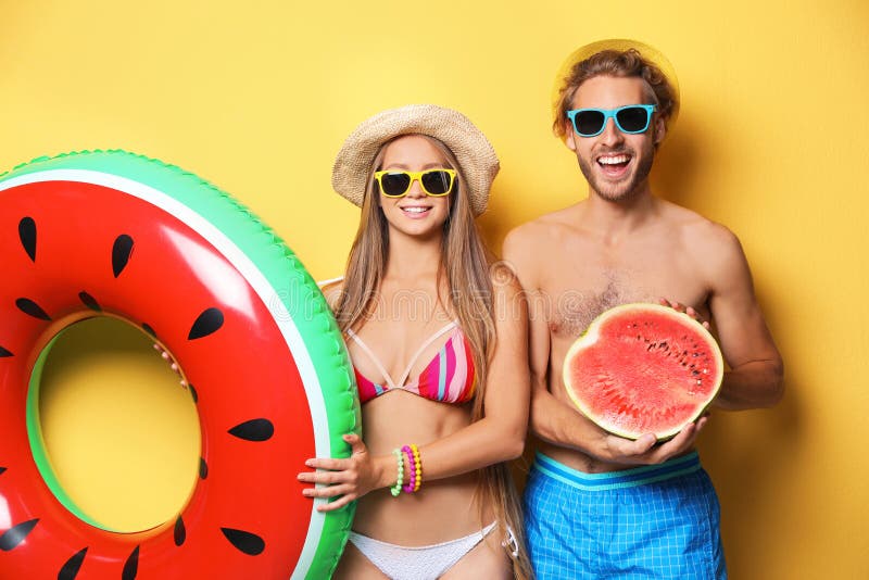 年轻情侣穿着沙滩装，拿着充气圈和西瓜 库存照片