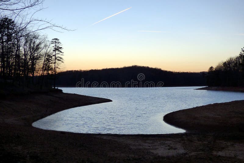 Winter sunset on Lake Lanier, Georgia in mid-winter appears to turn normally blue water into a silver reflection, accented by the natural depth curves of the man-made shoreline. This creates a beautiful winter travel destination. Camping locations are situated along this this spot. Winter sunset on Lake Lanier, Georgia in mid-winter appears to turn normally blue water into a silver reflection, accented by the natural depth curves of the man-made shoreline. This creates a beautiful winter travel destination. Camping locations are situated along this this spot.