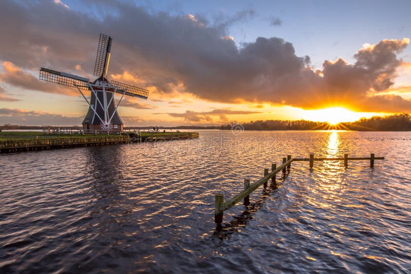 Tradional wooden windmill on banks of a lake under cloudy sunset in the netherlands. Tradional wooden windmill on banks of a lake under cloudy sunset in the netherlands